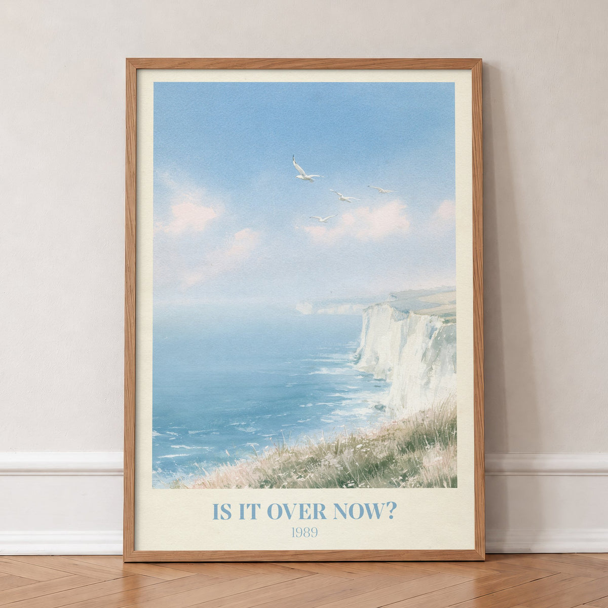 Is It Over Now? Taylor Swift print of white cliffs above a blue sea, in an oak frame, leaning against a wall on a herringbone floor