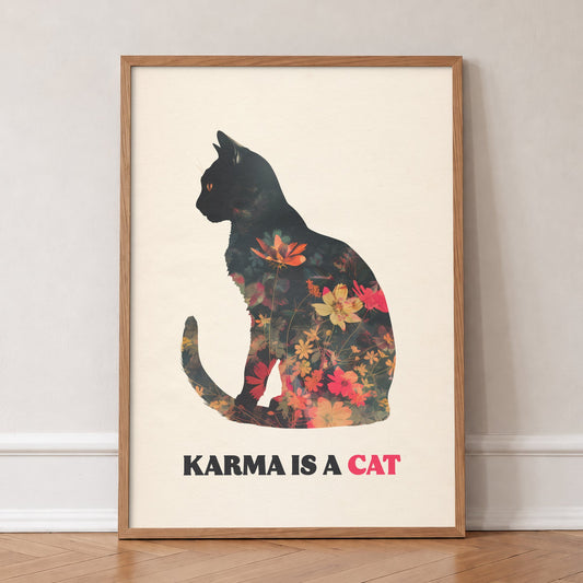 Karma Is A Cat Taylor Swift print of a black cat silhouette filled with red and orange flowers, in an oak frame, leaning against a wall on a herringbone floor