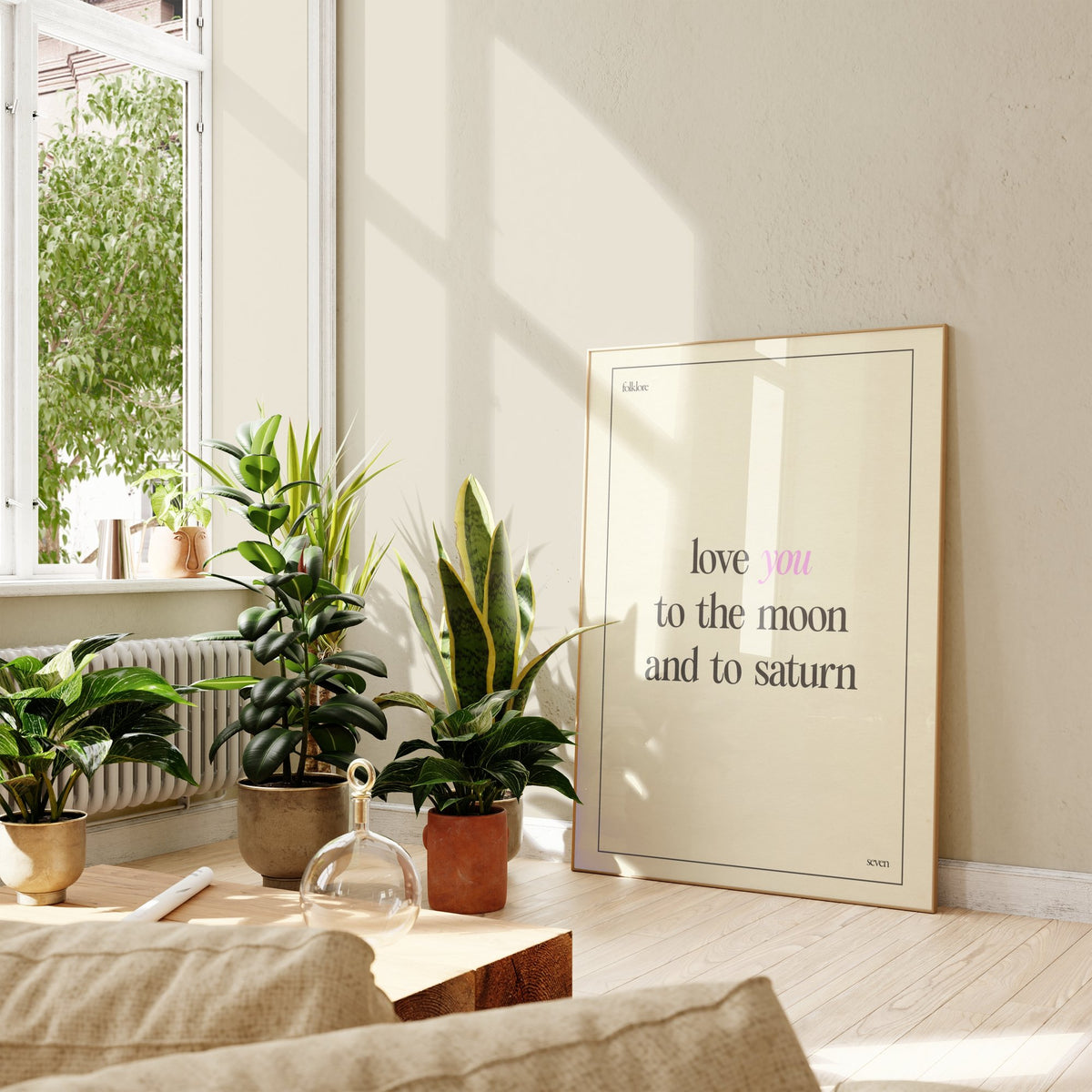 Love You To The Moon Taylor Swift print of the lyric in black and pink type on cream, framed, leaning against a wall beside potted plants