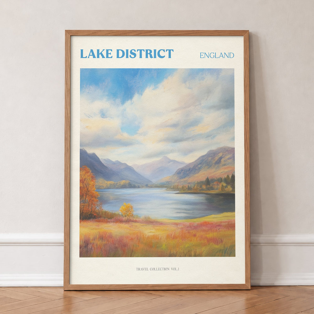 Lake District travel print of a lake between mountains under big clouds, with orange autumn grass, in an oak frame, leaning against a wall on a herringbone floor