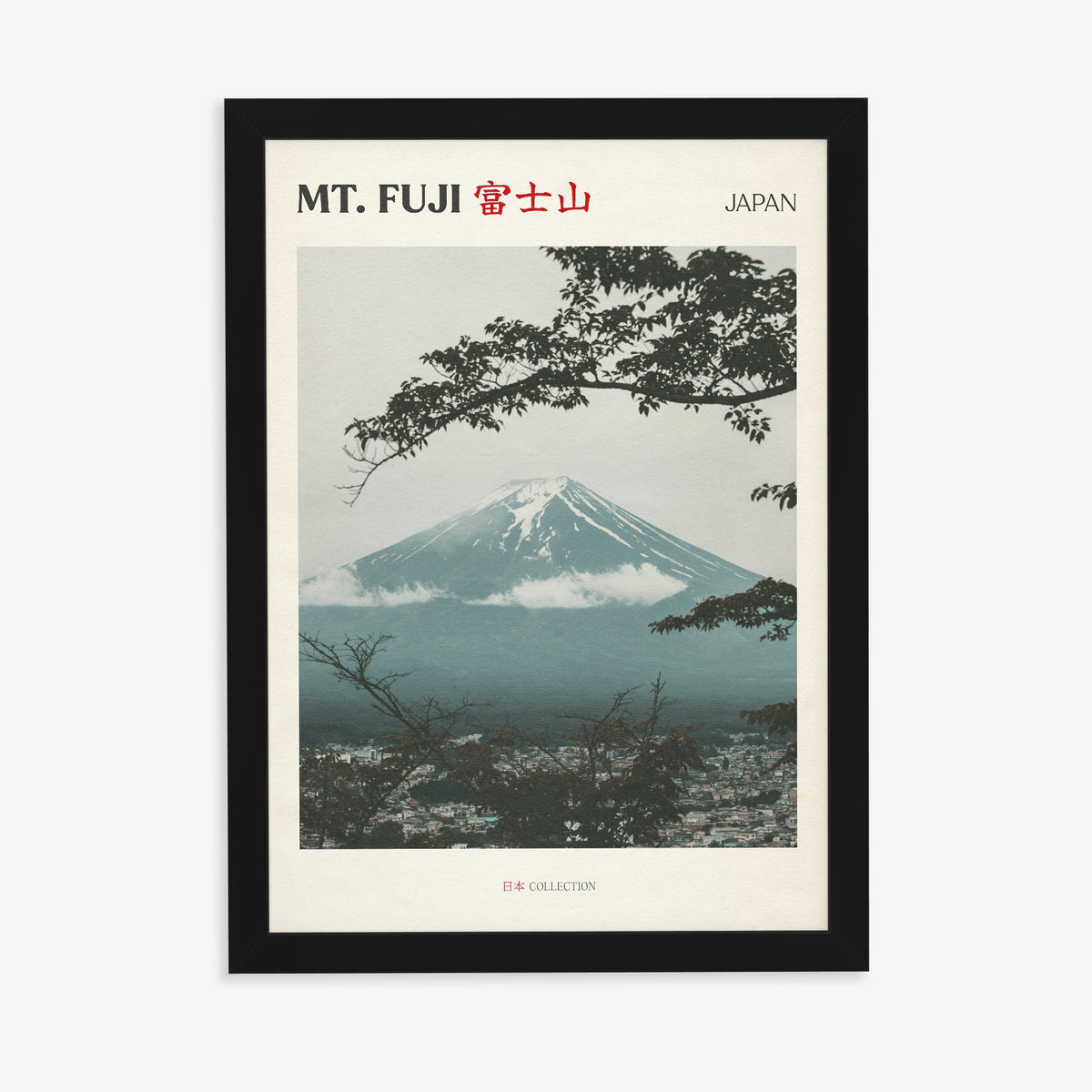 Mt Fuji travel print of snow-capped Mt Fuji framed by dark tree branches above a misty town, in a black frame on a plain wall