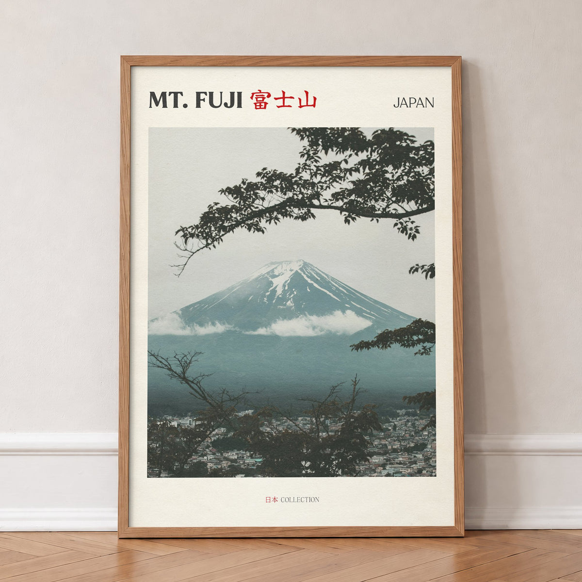 Mt Fuji travel print of snow-capped Mt Fuji framed by dark tree branches above a misty town, in an oak frame, leaning against a wall on a herringbone floor