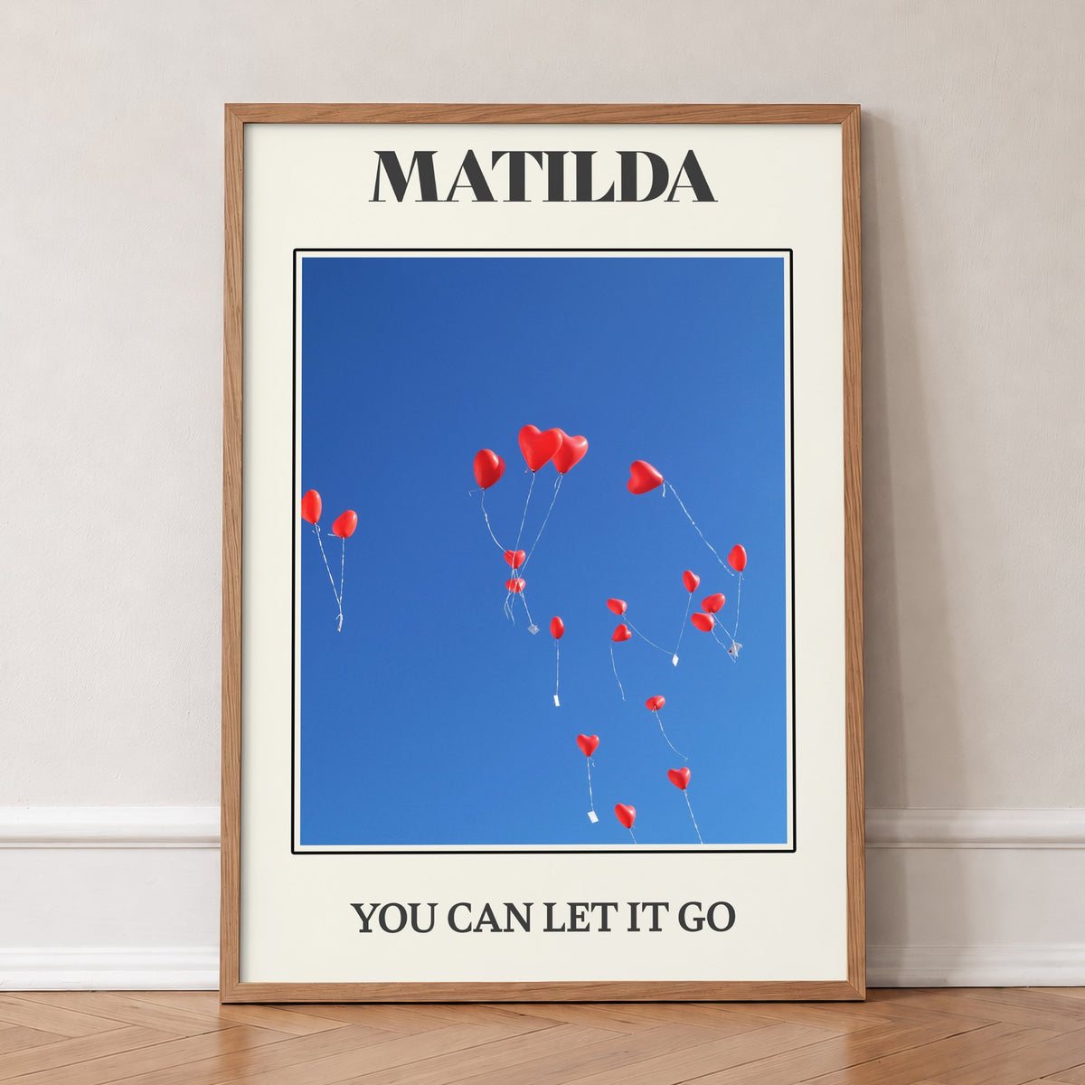 Matilda Harry Styles print of red heart balloons in a deep blue sky, in an oak frame, leaning against a wall on a herringbone floor
