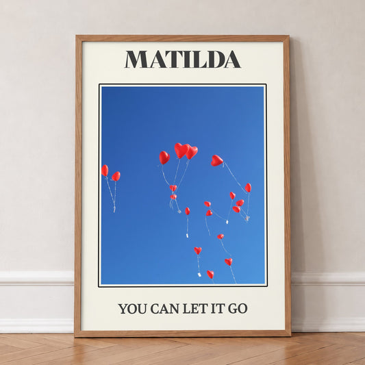 Matilda Harry Styles print of red heart balloons in a deep blue sky, in an oak frame, leaning against a wall on a herringbone floor