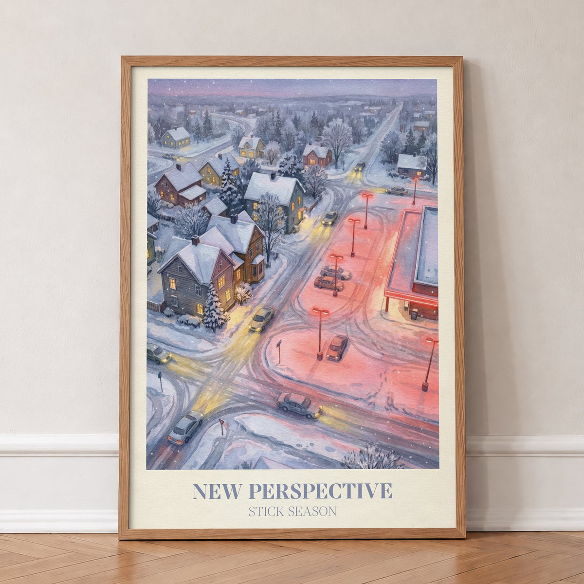 New Perspective Noah Kahan print of a snowy small town at night with a red-lit car park, in an oak frame, leaning against a wall on a herringbone floor