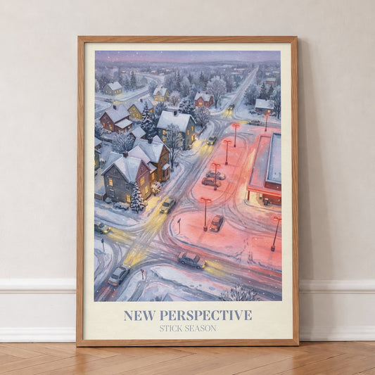 New Perspective Noah Kahan print of a snowy small town at night with a red-lit car park, in an oak frame, leaning against a wall on a herringbone floor