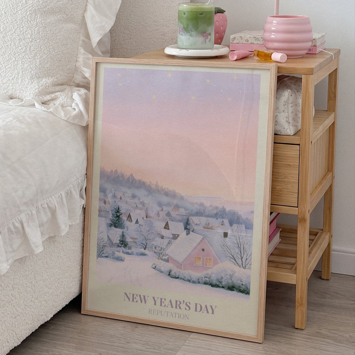 New Year’s Day Taylor Swift print of a snowy pink cottage, leaning beside a bed and a bamboo nightstand
