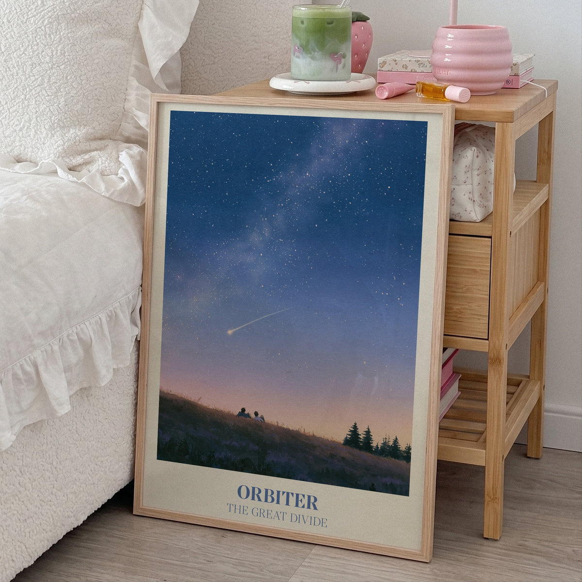 Orbiter Noah Kahan print of two people watching a shooting star from a hillside, leaning beside a bed and a bamboo nightstand