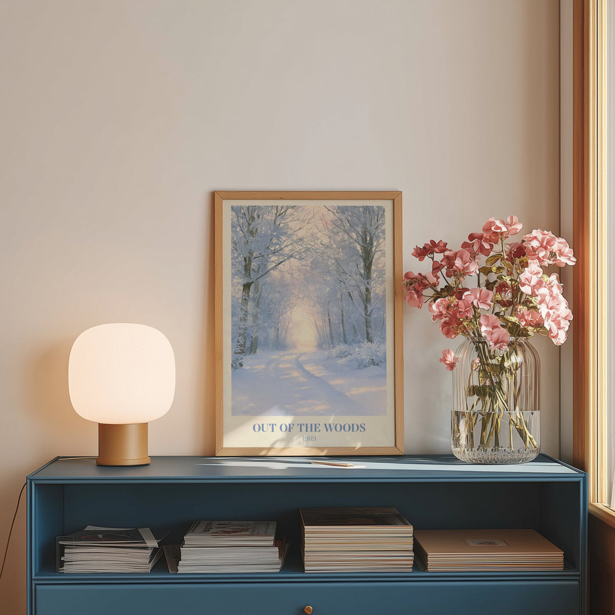 Out Of The Woods Winter Taylor Swift print of a snowy woodland path, on a blue sideboard with a lamp and flowers