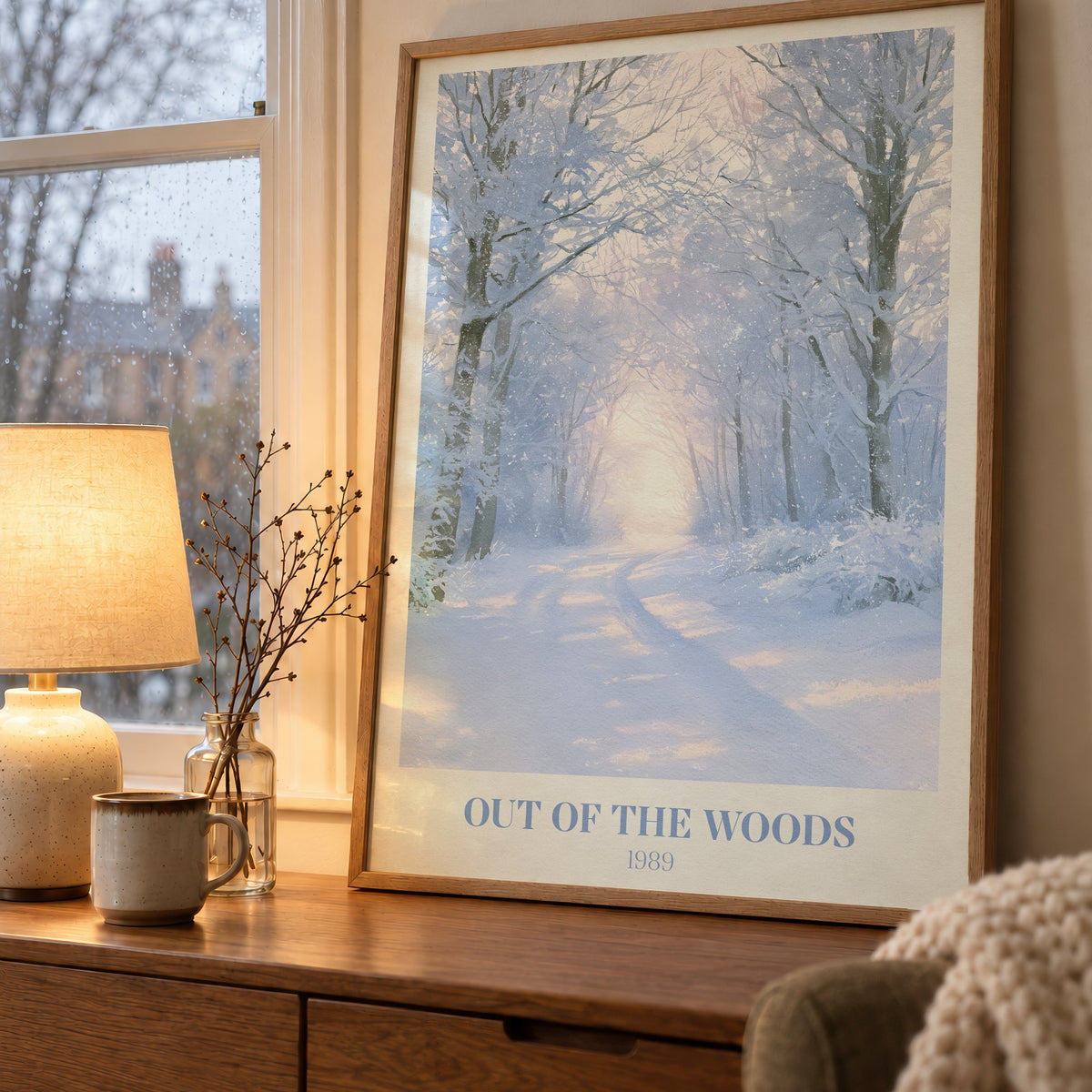 Out Of The Woods Winter Taylor Swift print of a snowy woodland path, on a wooden sideboard by a rainy window