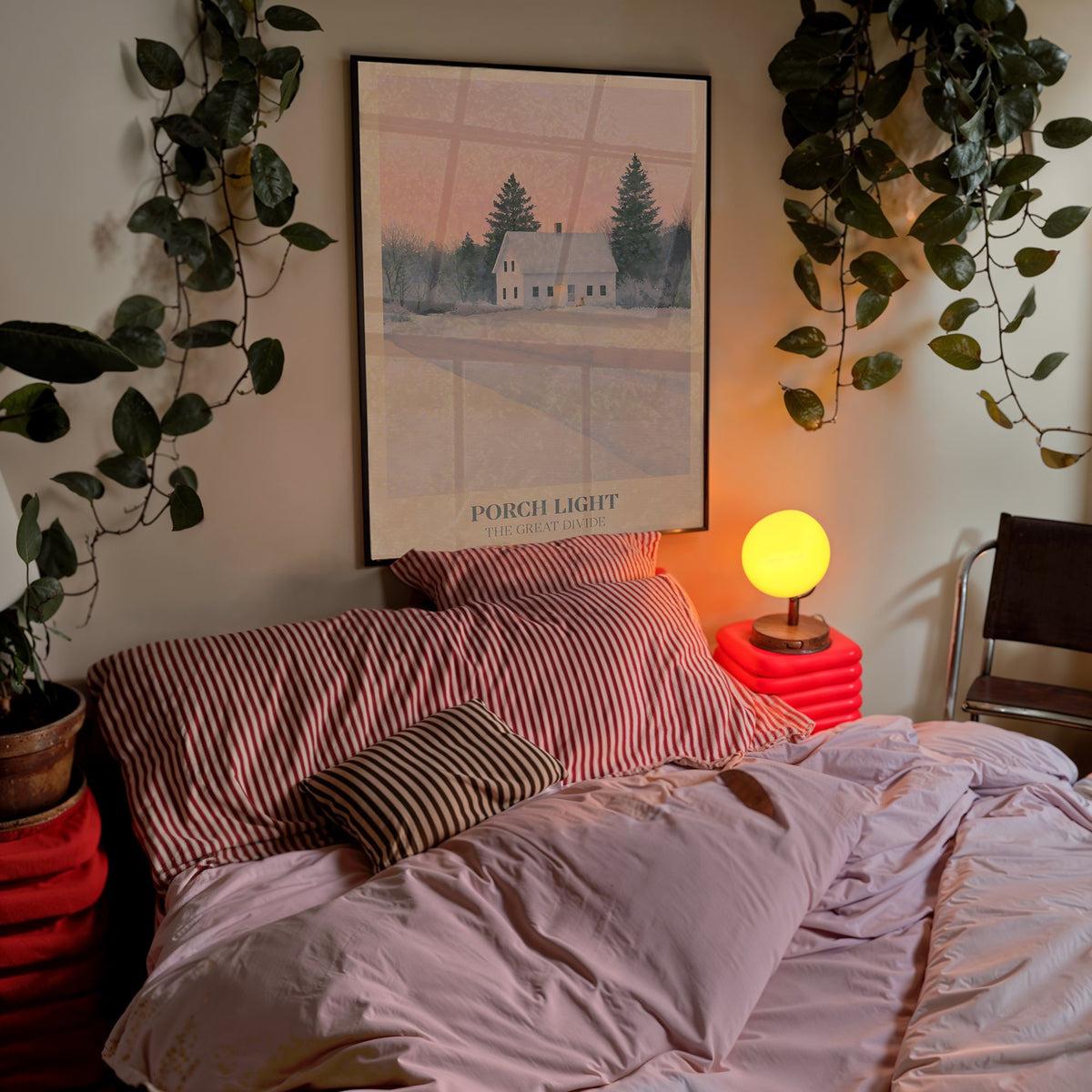 Porch Light Noah Kahan print of a snowy farmhouse, porch light on, framed above a bed with trailing plants