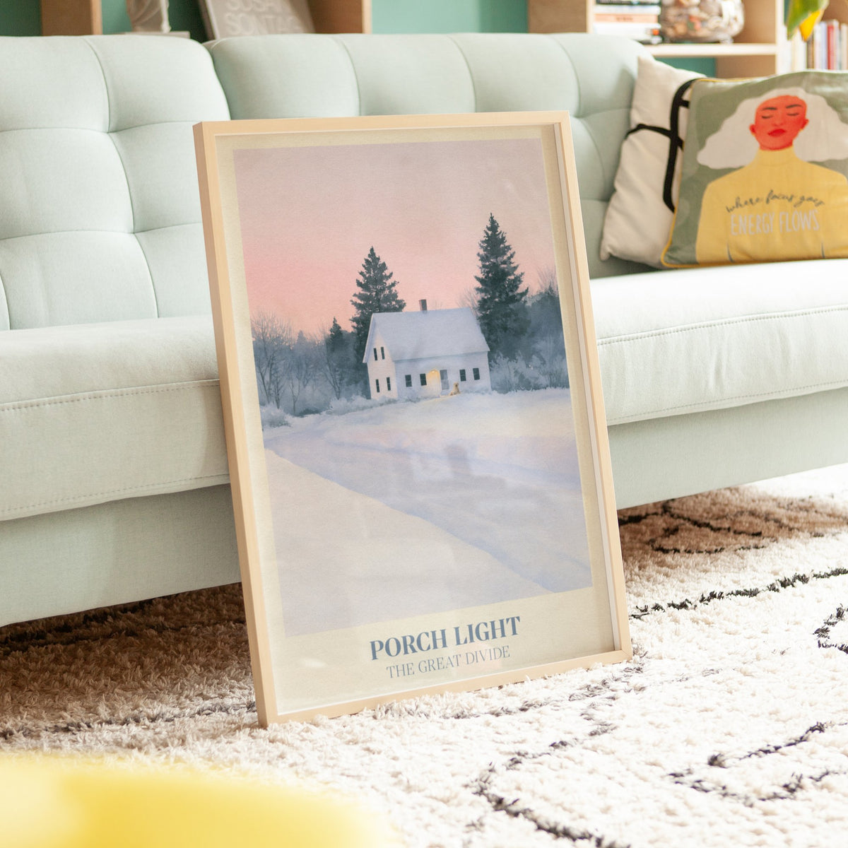Porch Light Noah Kahan print of a snowy farmhouse, porch light on, framed, leaning against a mint sofa