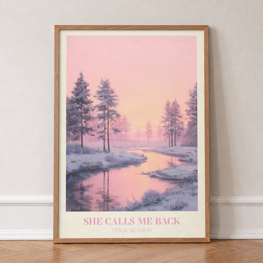She Calls Me Back Noah Kahan print of a frosty river winding between pines under a pink sky, in an oak frame, leaning against a wall on a herringbone floor