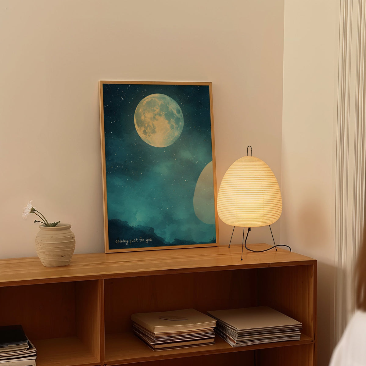 Shining Just For You Taylor Swift print of a full moon over a starry blue night sky, framed on a shelf beside a paper lantern