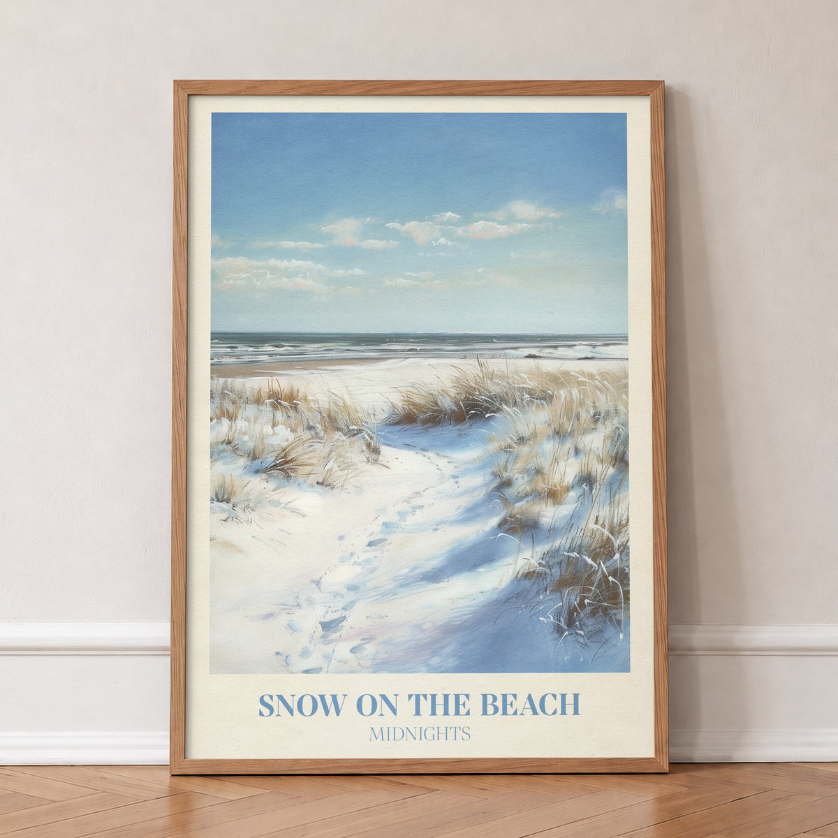 Snow On The Beach Taylor Swift print of snowy sand dunes and beach grass beside a blue sea, in an oak frame, leaning against a wall on a herringbone floor