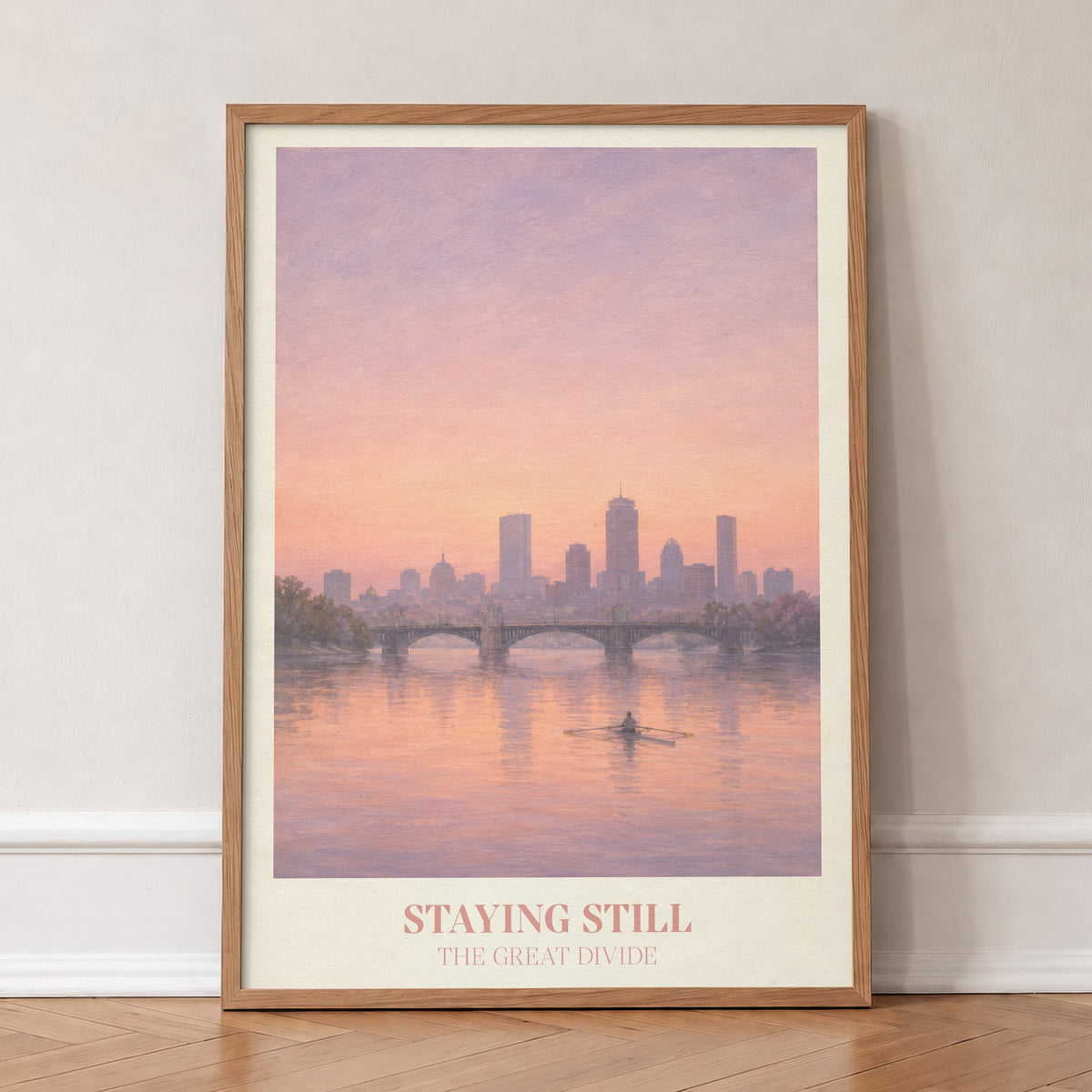 Staying Still Noah Kahan print of a lone rower on a pink river below a city skyline, in an oak frame, leaning against a wall on a herringbone floor