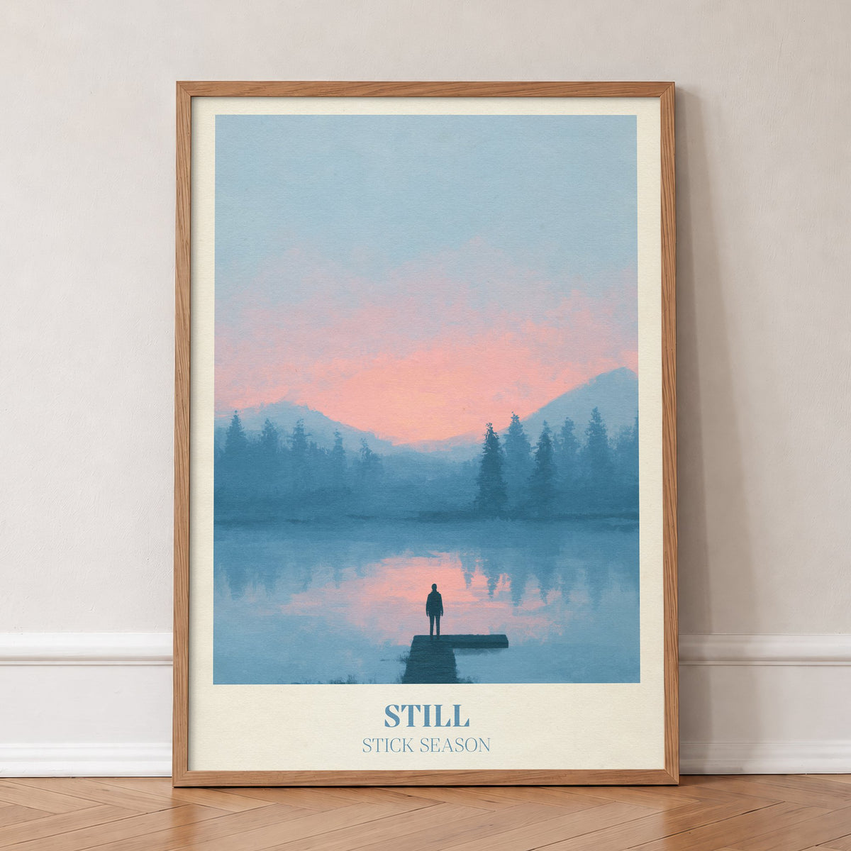Still Noah Kahan print of a lone figure on a jetty over a pink and blue lake, in an oak frame, leaning against a wall on a herringbone floor