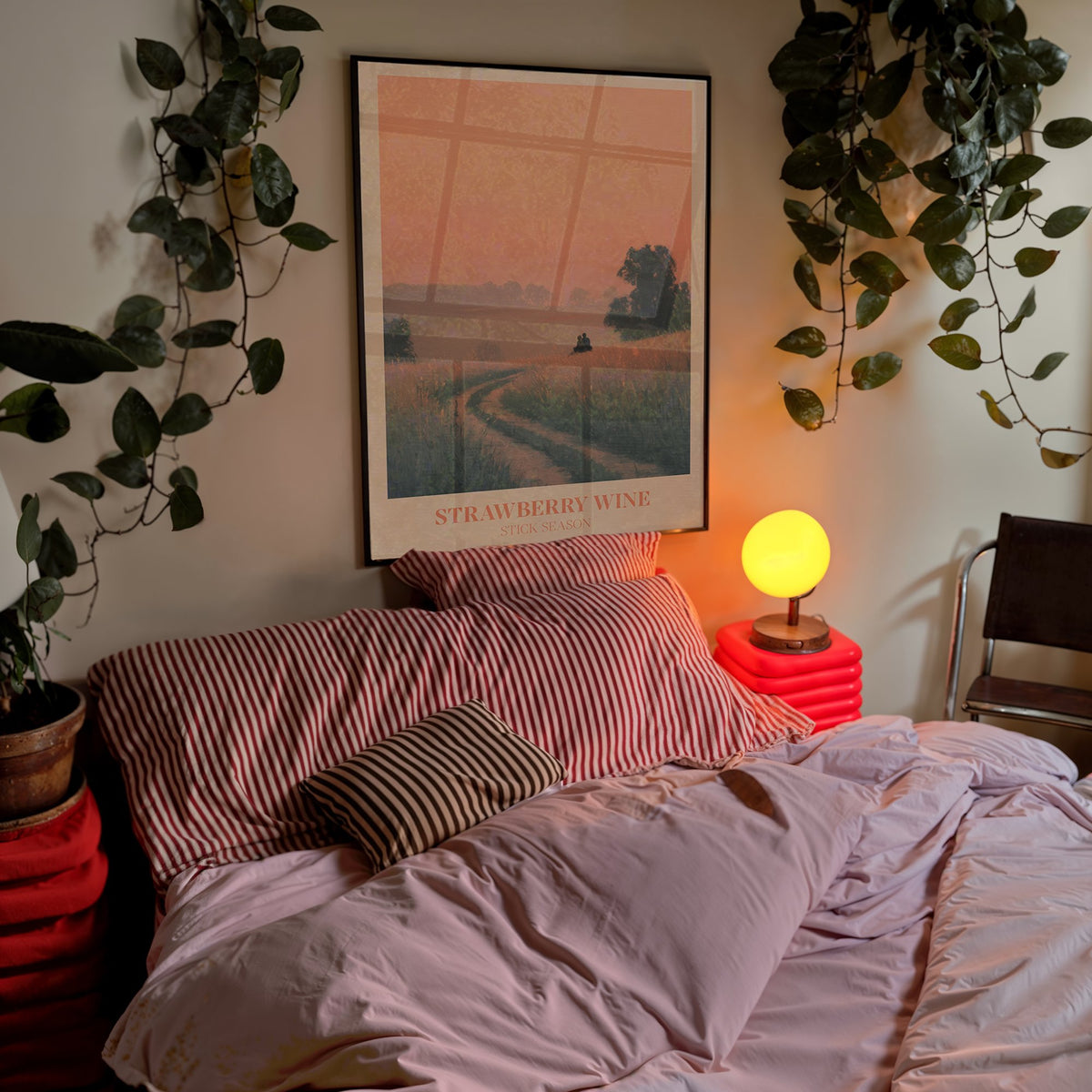Strawberry Wine Noah Kahan print of two figures in a golden meadow under a peach sky, framed above a bed with trailing plants