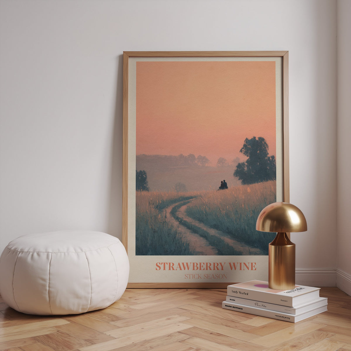 Strawberry Wine Noah Kahan print of two figures in a golden meadow under a peach sky, framed beside a white pouffe