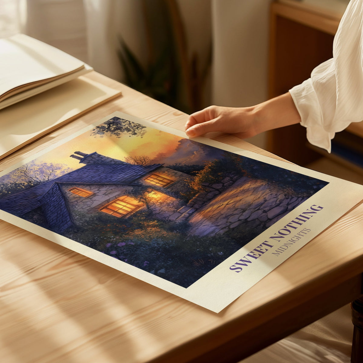 Sweet Nothing Evening Cottage Taylor Swift print of a stone cottage with glowing windows at dusk, laid flat on a sunny table