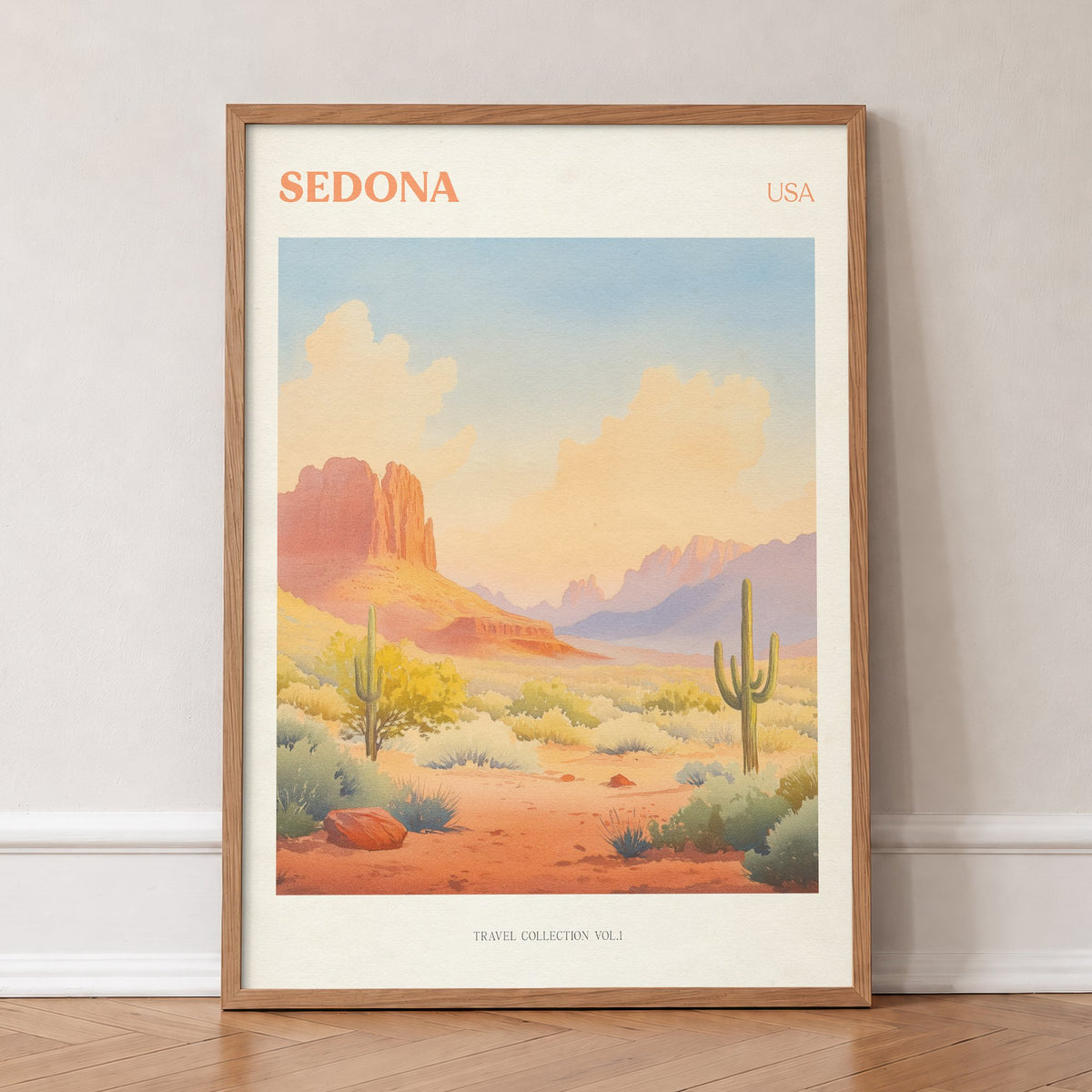 Sedona travel print of red rock formations and tall cacti under a peach desert sky, in an oak frame, leaning against a wall on a herringbone floor