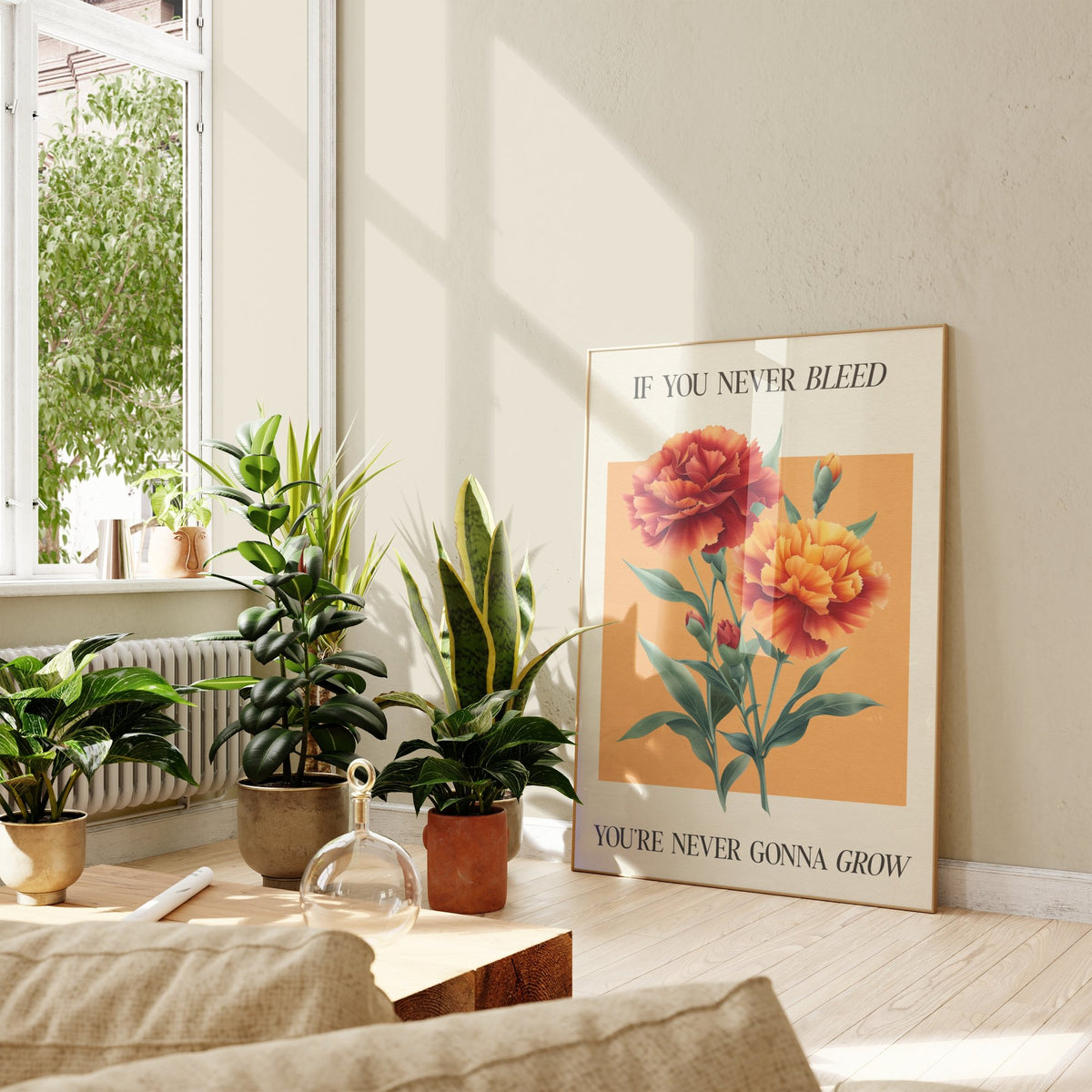 The 1 Botanical Taylor Swift print of red and orange carnations on a peach square, framed, leaning against a wall beside potted plants