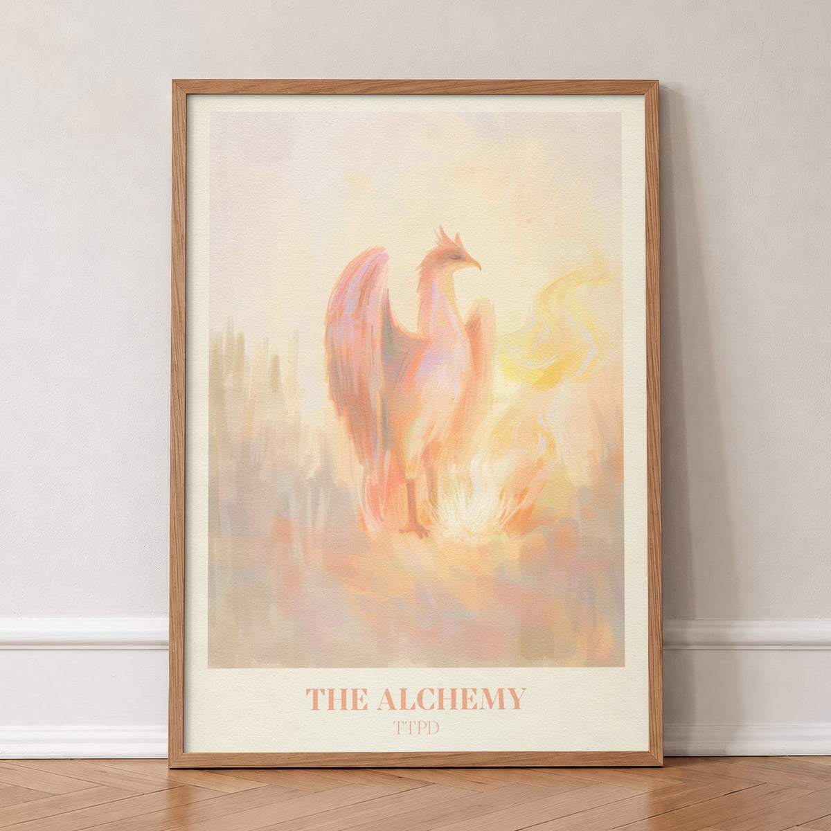 The Alchemy Taylor Swift print of a pink and peach phoenix rising beside golden flames, in an oak frame, leaning against a wall on a herringbone floor
