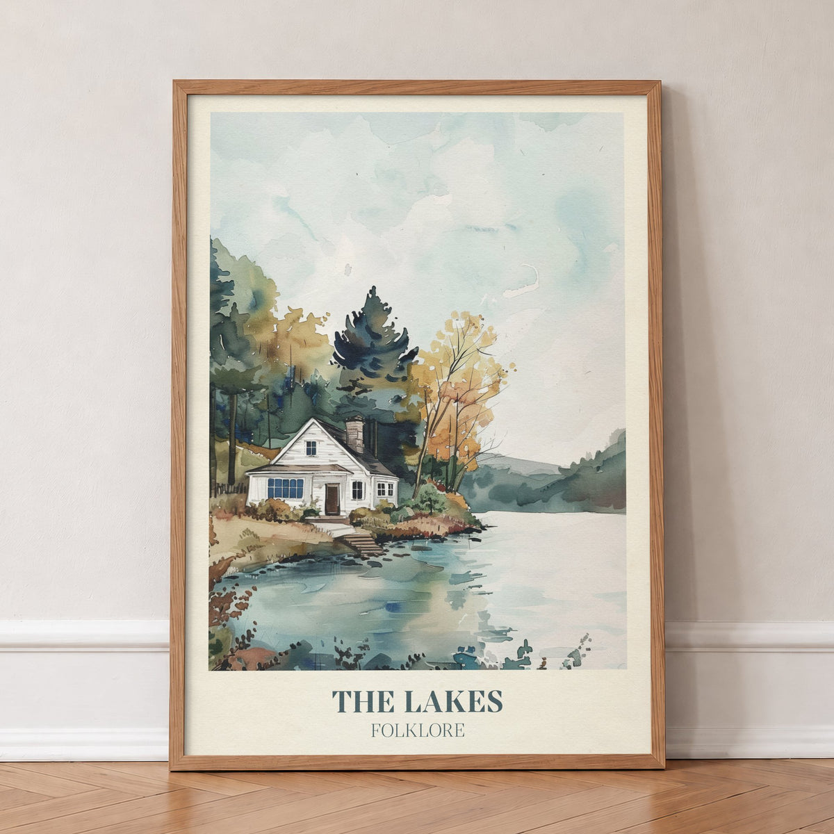 The Lakes Taylor Swift print of a white cottage beside a still lake and trees, in an oak frame, leaning against a wall on a herringbone floor