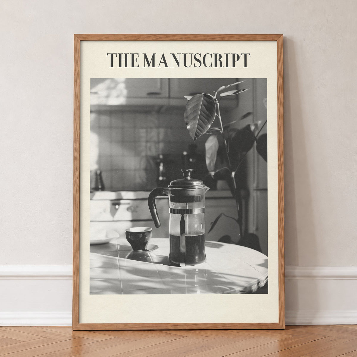 The Manuscript Taylor Swift print of a black and white French press and cup on a sunlit table, in an oak frame, leaning against a wall on a herringbone floor