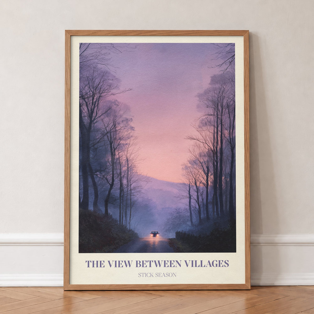 The View Between Villages Noah Kahan print of headlights on a misty road through purple trees, in an oak frame, leaning against a wall on a herringbone floor