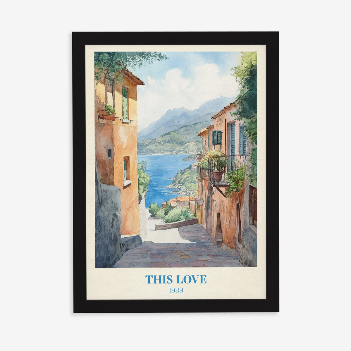 This Love Taylor Swift print of a stone lane between terracotta houses down to a blue bay, in a black frame on a plain wall