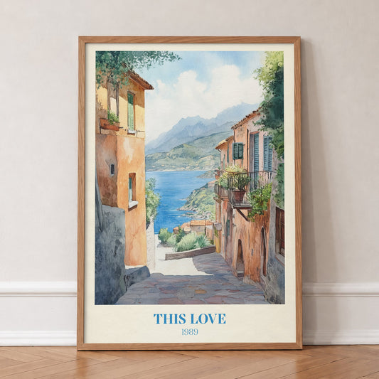 This Love Taylor Swift print of a stone lane between terracotta houses down to a blue bay, in an oak frame, leaning against a wall on a herringbone floor