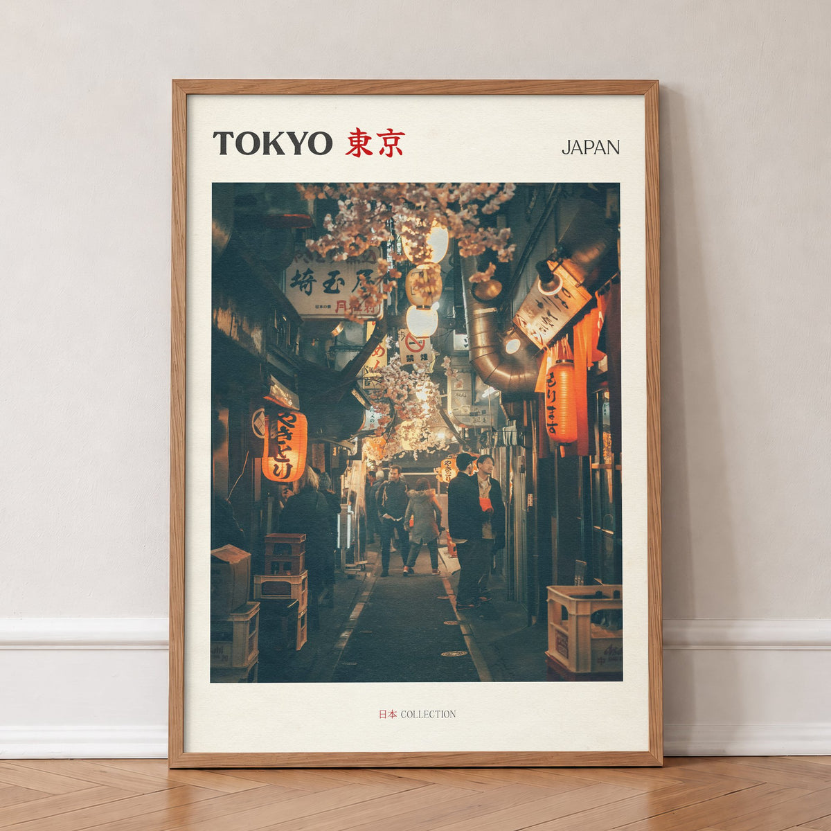 Tokyo travel print of a narrow side street at night lit by red paper lanterns, in an oak frame, leaning against a wall on a herringbone floor