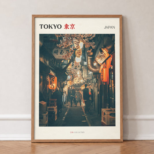 Tokyo travel print of a narrow side street at night lit by red paper lanterns, in an oak frame, leaning against a wall on a herringbone floor