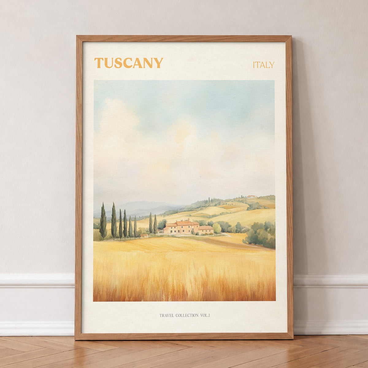 Tuscany travel print of a hilltop farmhouse above golden wheat fields and cypress trees, in an oak frame, leaning against a wall on a herringbone floor