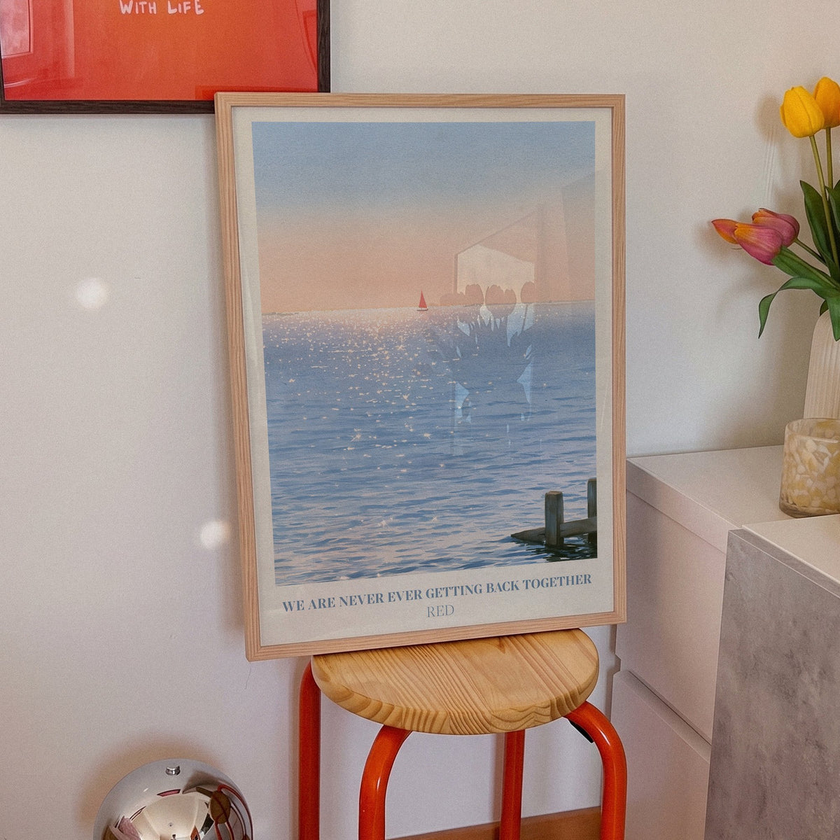 We Are Never Ever Getting Back Together Taylor Swift print of a red sailboat, on an orange stool beside tulips