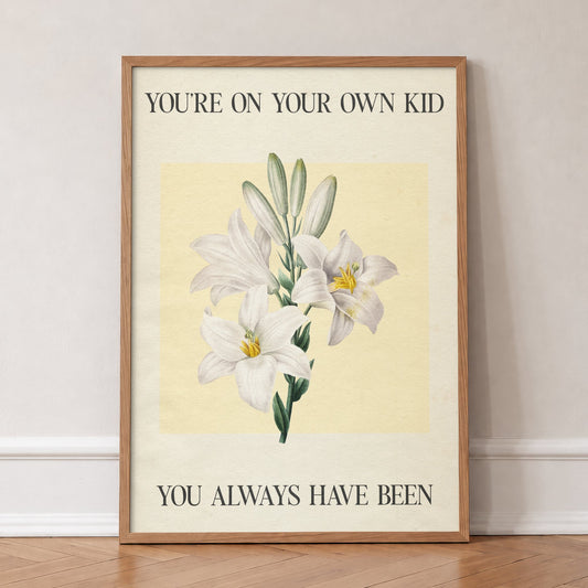 You’re On Your Own Kid Botanical Taylor Swift lyric print of white lilies on yellow, in an oak frame, leaning against a wall on a herringbone floor