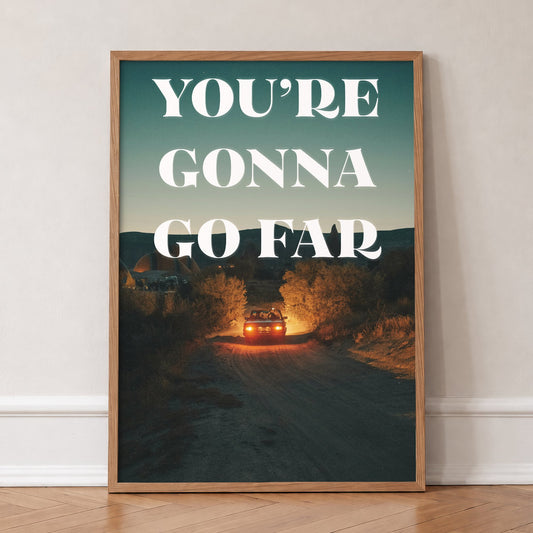 You're Gonna Go Far Noah Kahan print with bold white lettering over dark hills at dusk, in an oak frame, leaning against a wall on a herringbone floor